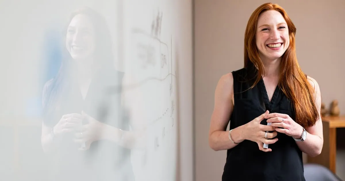 A woman in her early 30s writing career-change plans on a whiteboard in a bright office