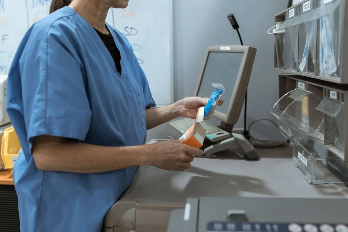 A healthcare worker in scrubs retrieving supplies from a shelf in a clinical storage room