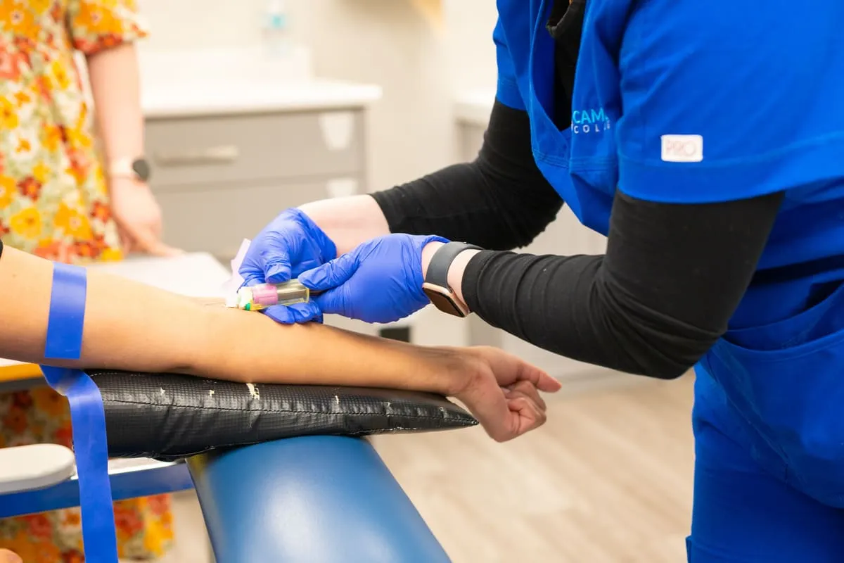 A healthcare worker performing a blood draw on a seated patient's arm in a clinic setting